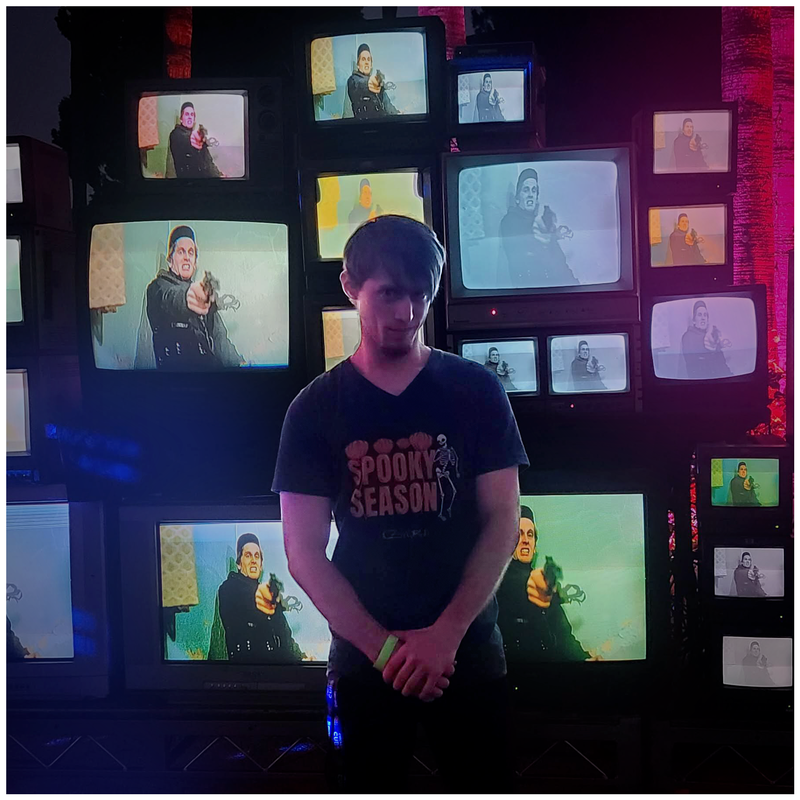 Zac smiling deviously in front of a stack of 90s TV monitors displaying horror content.